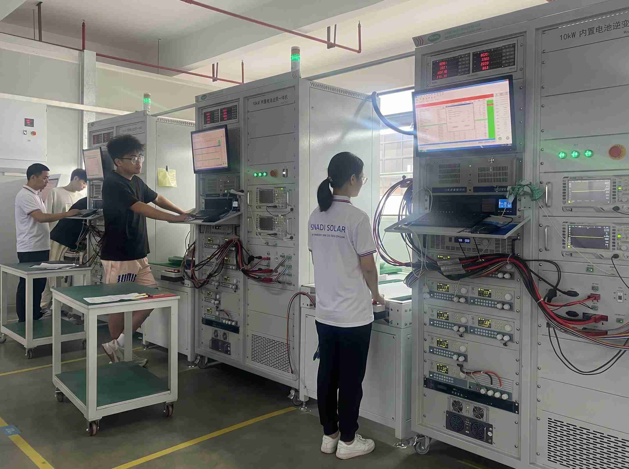Técnicos de SNADI con uniformes de marca realizando pruebas de control de calidad en sistemas de almacenamiento de energía residencial en un laboratorio profesional de fábrica solar.