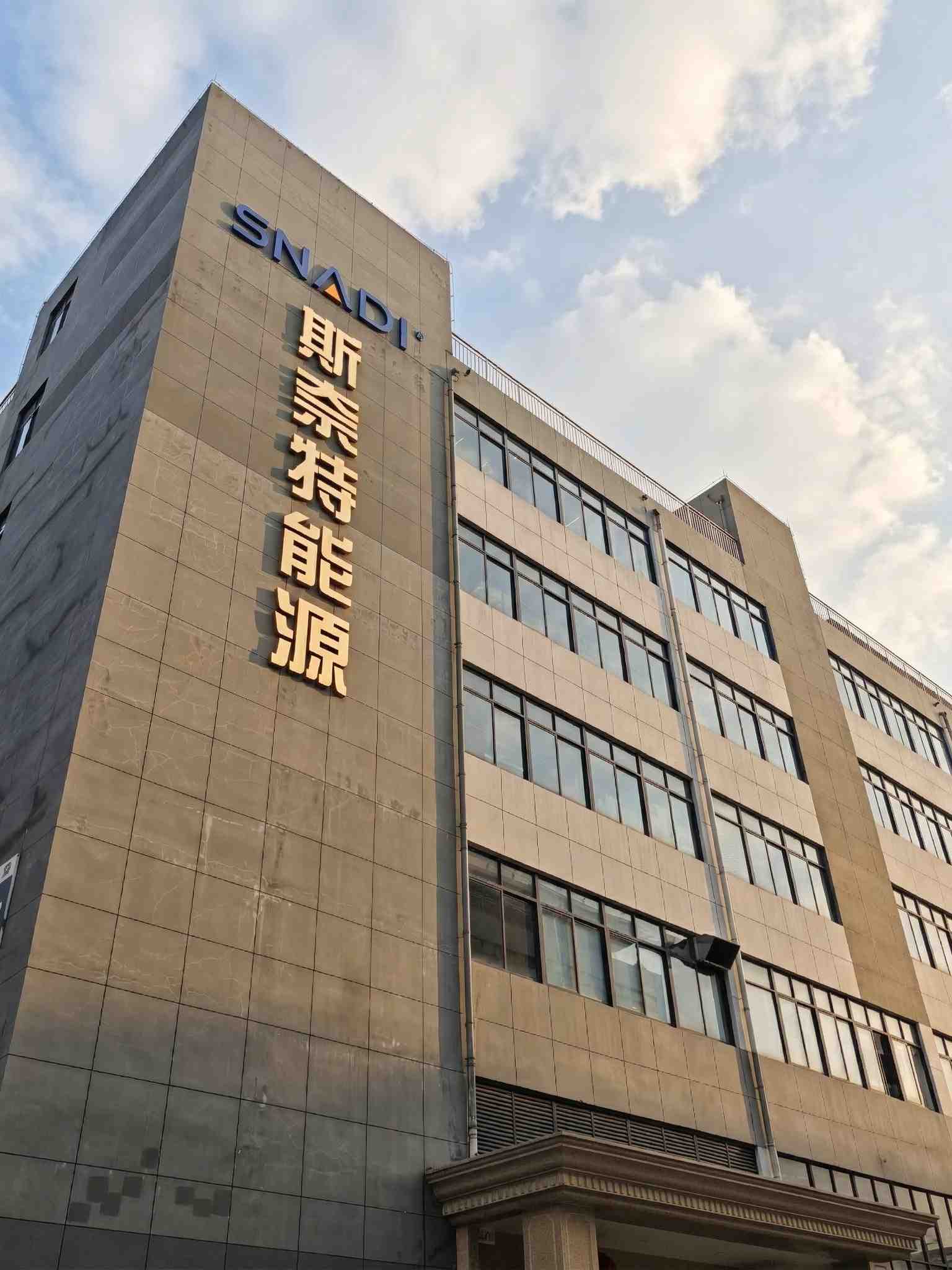 一座现代化的多层SNADI可再生能源解决方案公司建筑，灰色建筑，顶部是SNADI标志，下面是金色的中文字“斯奈特能源”，映衬着晴朗的天空。
